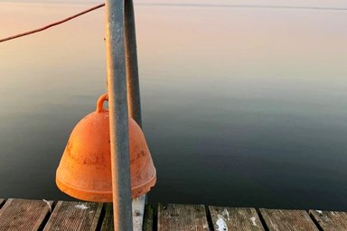 Orange-colored bell on the jetty in front of a calm lake