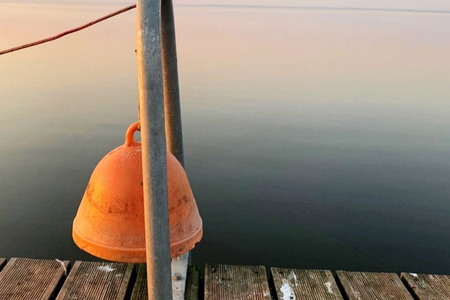 Orange-colored bell on the jetty in front of a calm lake