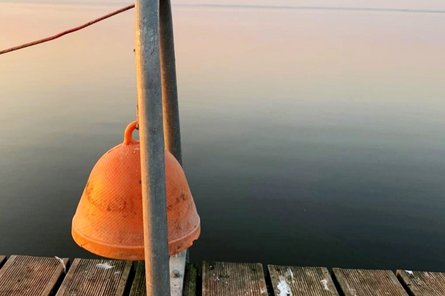 Orange-colored bell on the jetty in front of a calm lake
