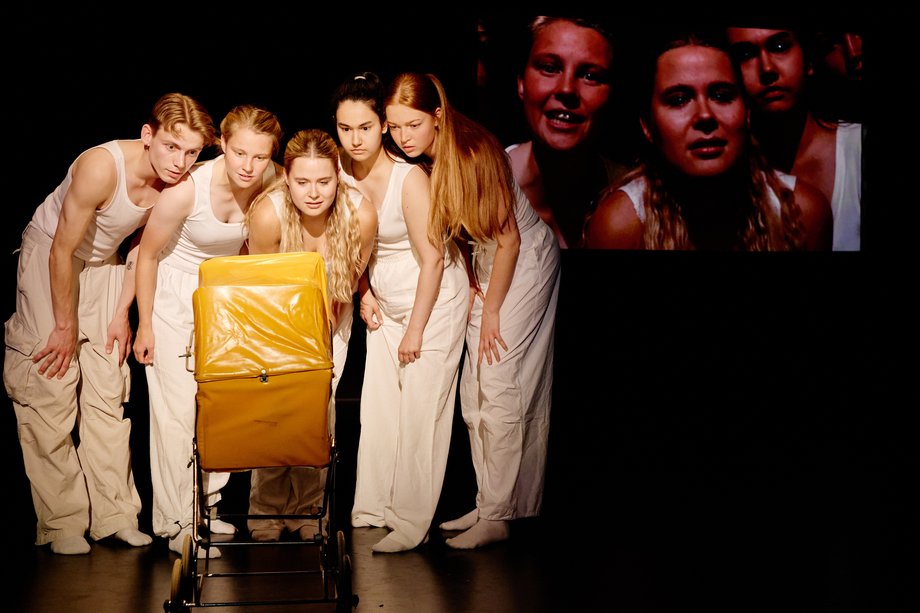 Alles noch im Rahmen (Semesterabschluss 2025, Lehramt Theater) Eine Gruppe steht um einen gelben Kinderwagen und blickt hinein.