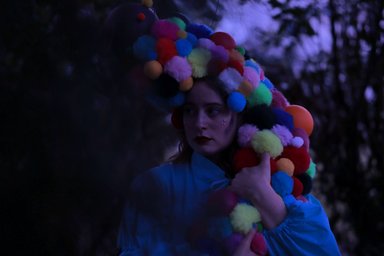 2026-03-20 Fete Galante Person mit bunter Perücke aus Kugeln in der Dämmerung