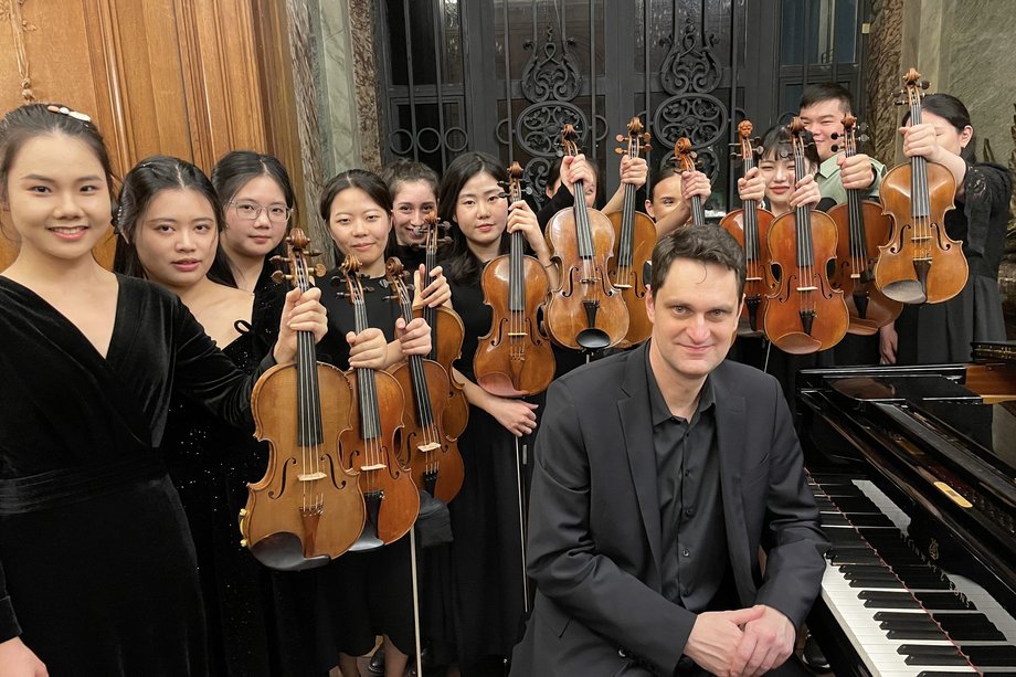 zwölf Violinist:innen und ein Pianist mit ihren Instrumenten