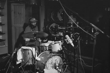 ein Mann am Schlagzeug; im Vordergrund mehrere Mikrofone