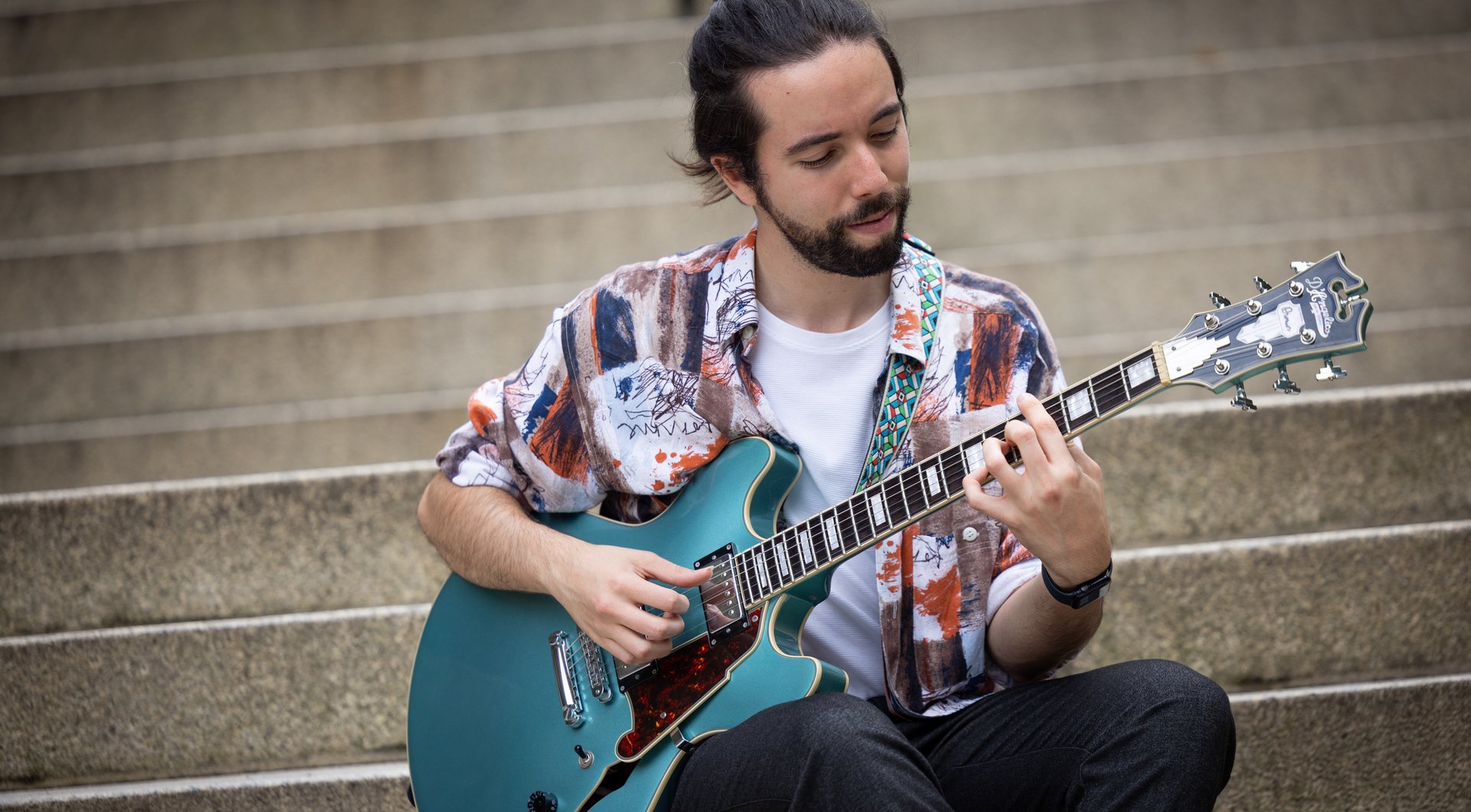 Mann sitzt mit E-Gitarre auf einer grauen Steintreppe und spielt