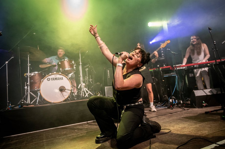 Popkurs 2025 Foto von einer Frau mit Band, die auf einer Bühne singt.