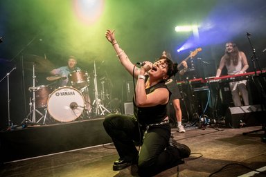 Popkurs 2025 Foto von einer Frau mit Band, die auf einer Bühne singt.