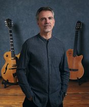 Roland Cabezas Porträt von Roland Cabezas mit zwei Gitarren im Hintergrund