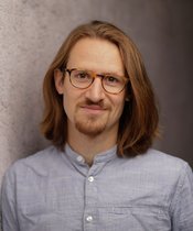 Portrait eine Mannes mit Brille und halblangen Haaren, hellblaues Hemd