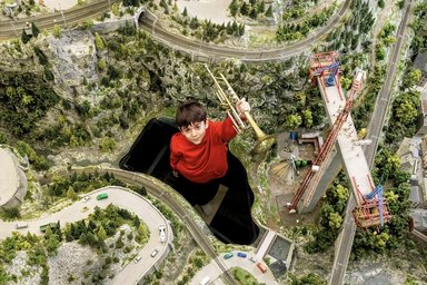 Stockhausen für Kinder - Michaels Reise 04-2026 Kind mit einer Trompete steht in einer Miniaturlandschaft; Ansicht von oben
